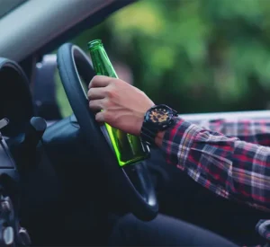 A person driving, while holding a beer bottle.