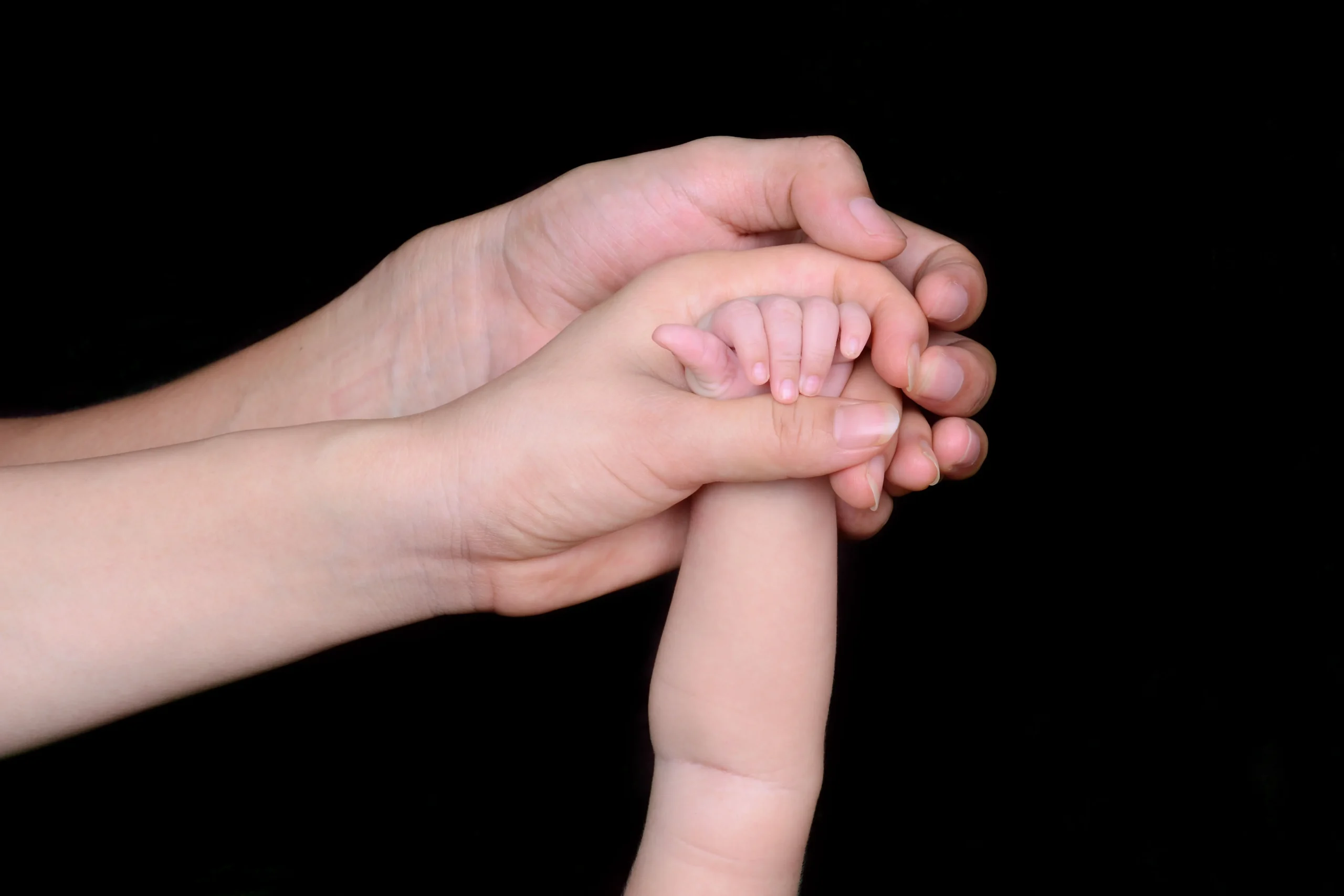 Mother and father hands holding baby's hand.