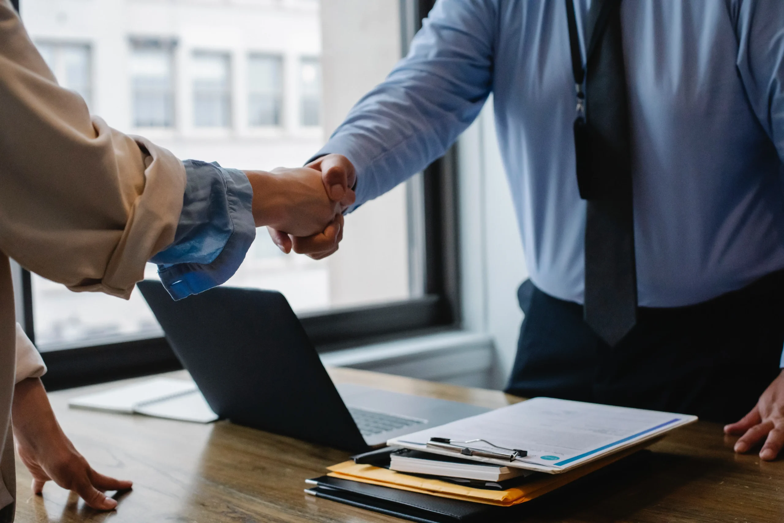 Divorce Lawyer and client shaking hands over a stack of paper work and a computer on a desk.