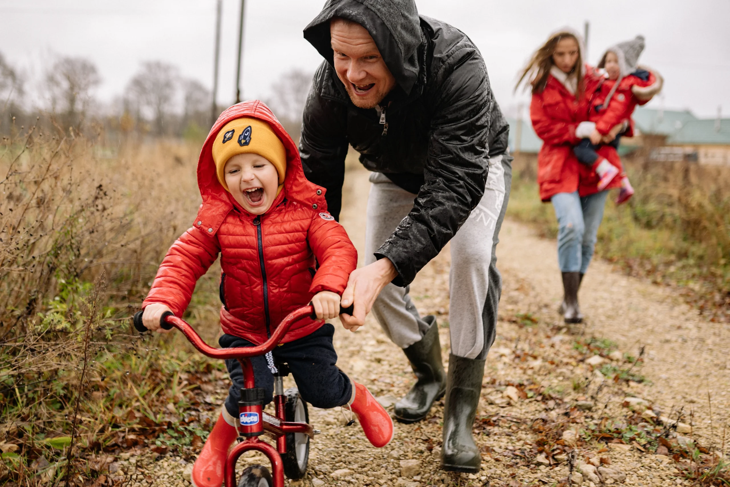 Father helping a child ride a bike and a mother holding a child in background