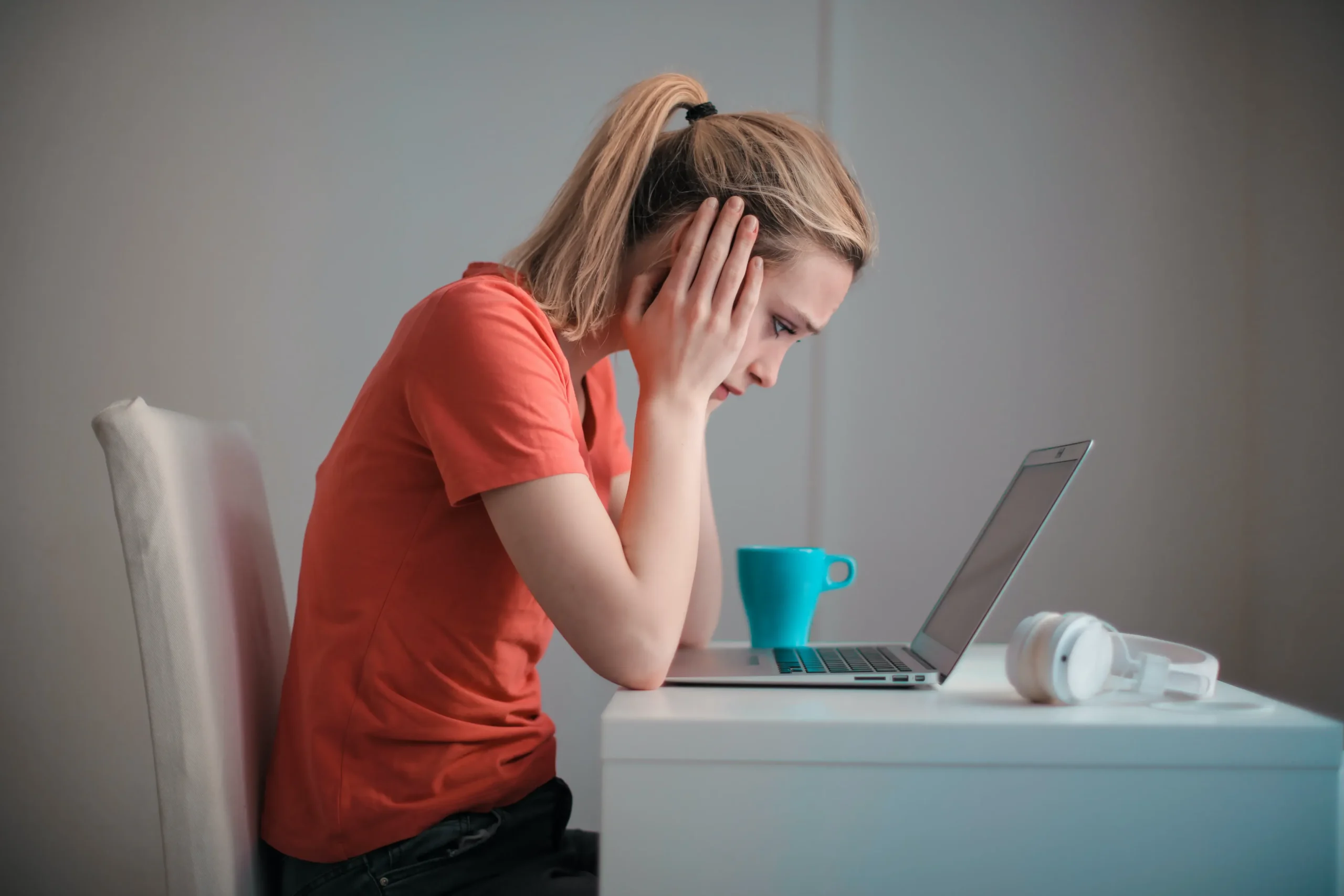 Women upset, sitting in front of a computer, holding her head.
