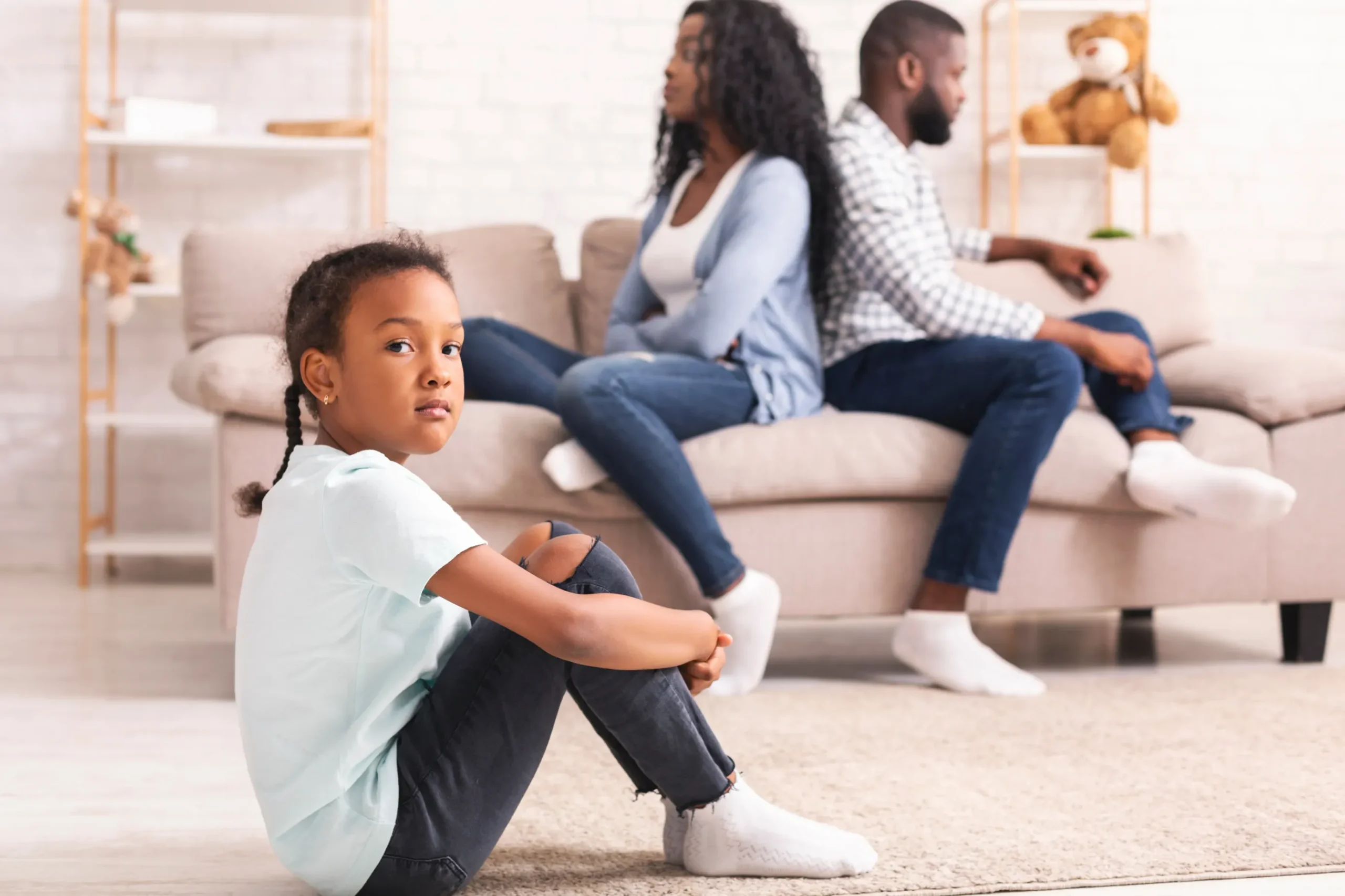 Parents are arguing in the background with a sad child.