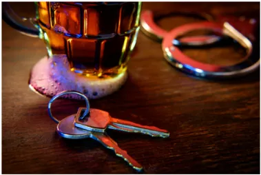 A drink on a bar with keys and handcuffs.