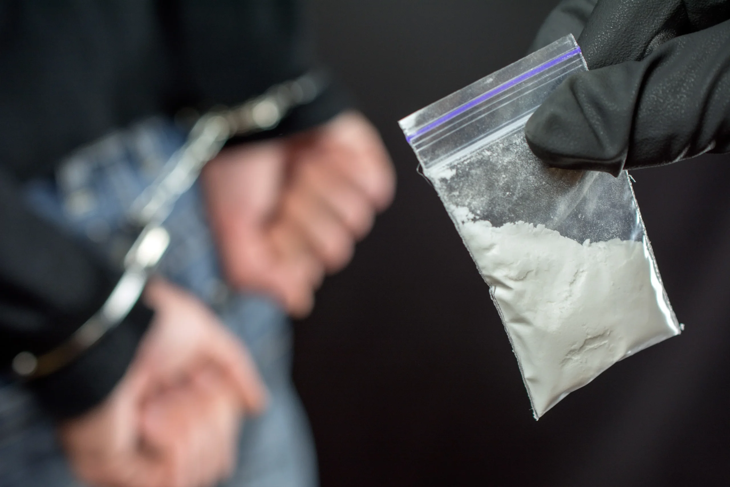 A person in handcuffs and a smart bag with a white powder.