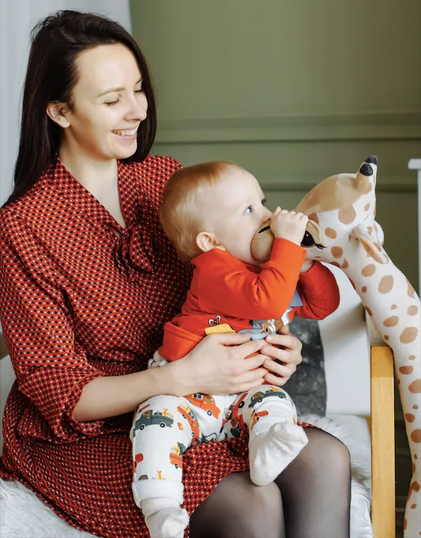 Woman holding baby who is chewing a stuffed giraffe.