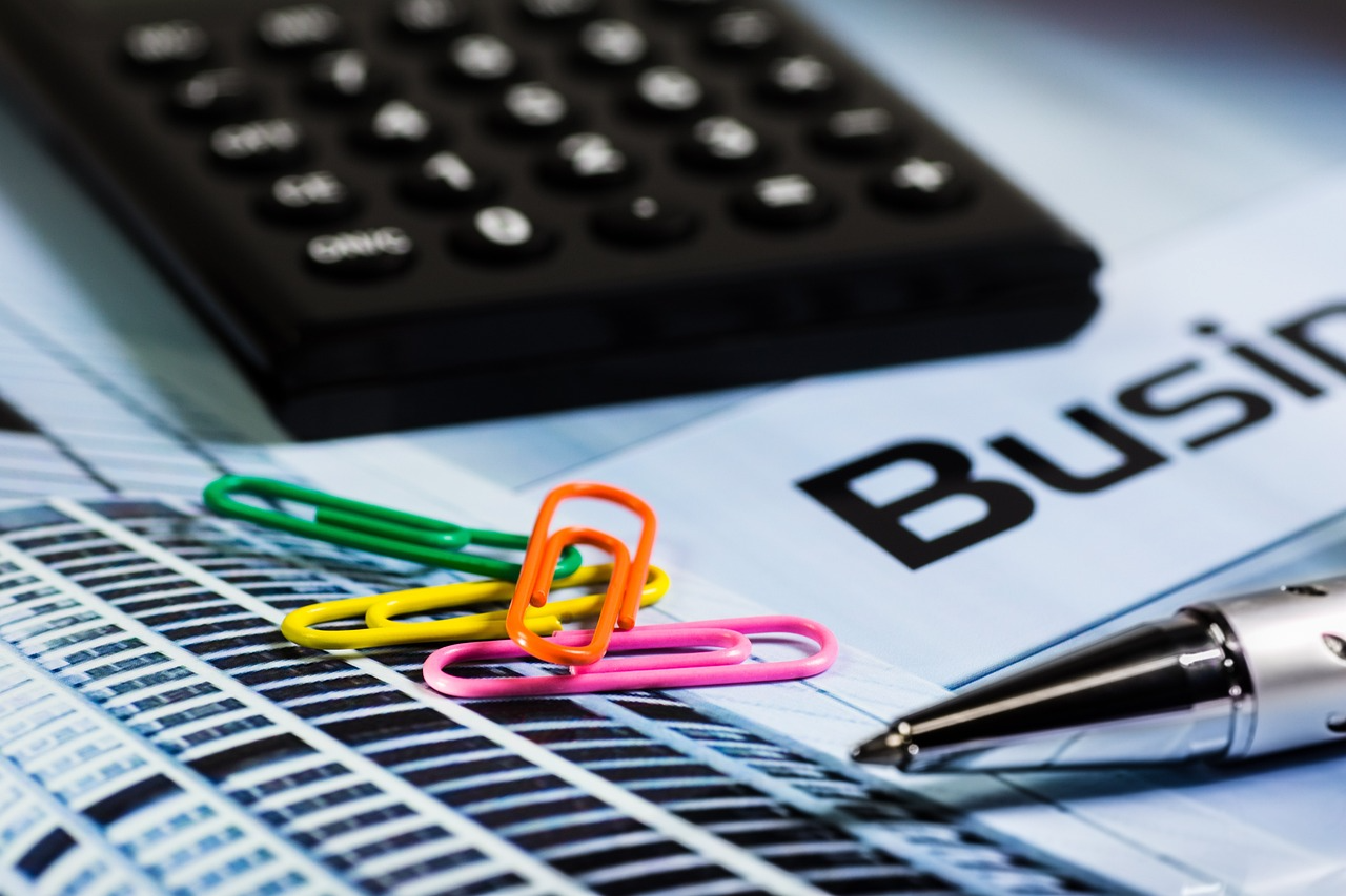 A black calculator and multi-color paperclips atop a stack of documents.