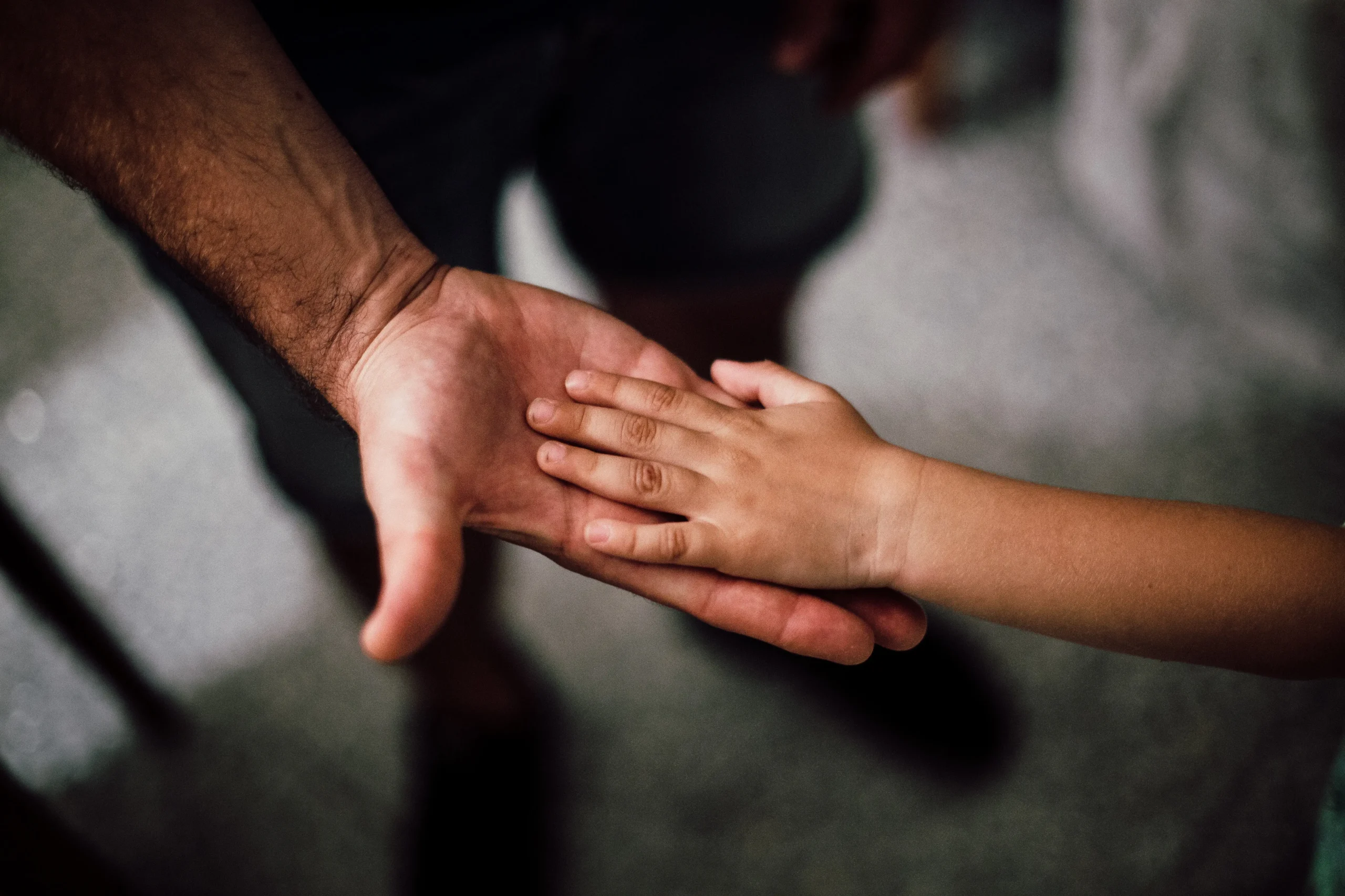 A close up image of a father and his young child holding hands.