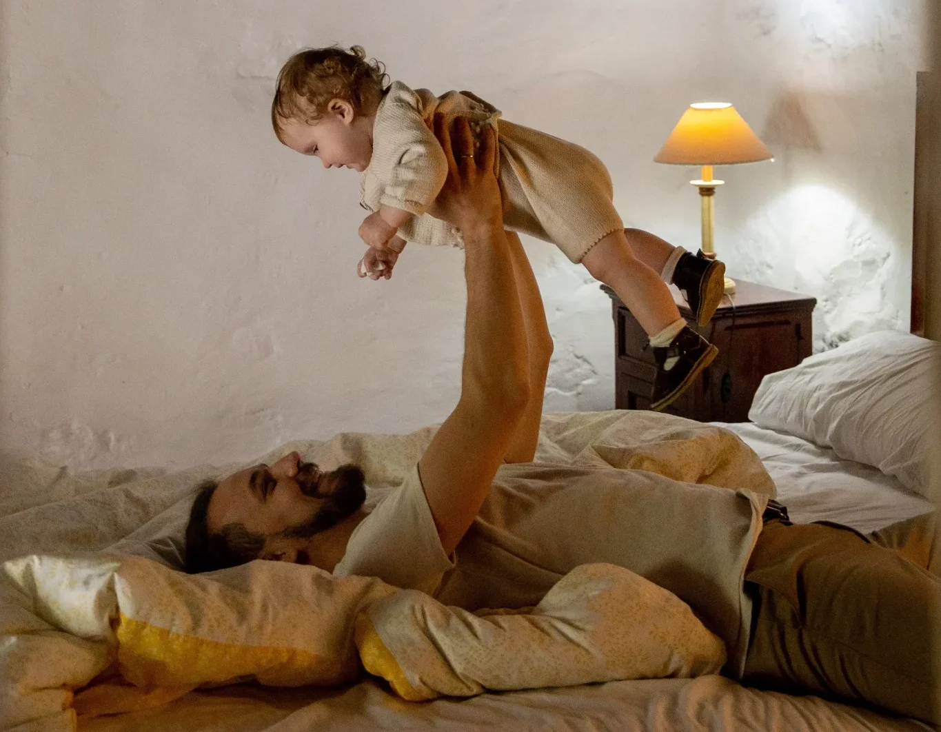 Father laying on his back on a bed while holding up his baby in the air.