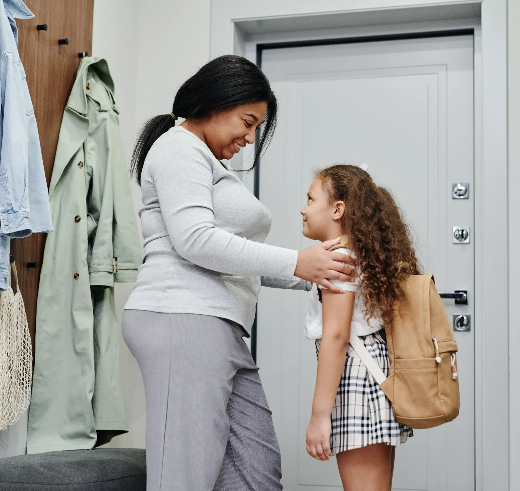 Mother helping her daughter put on her backpack and go off to school.