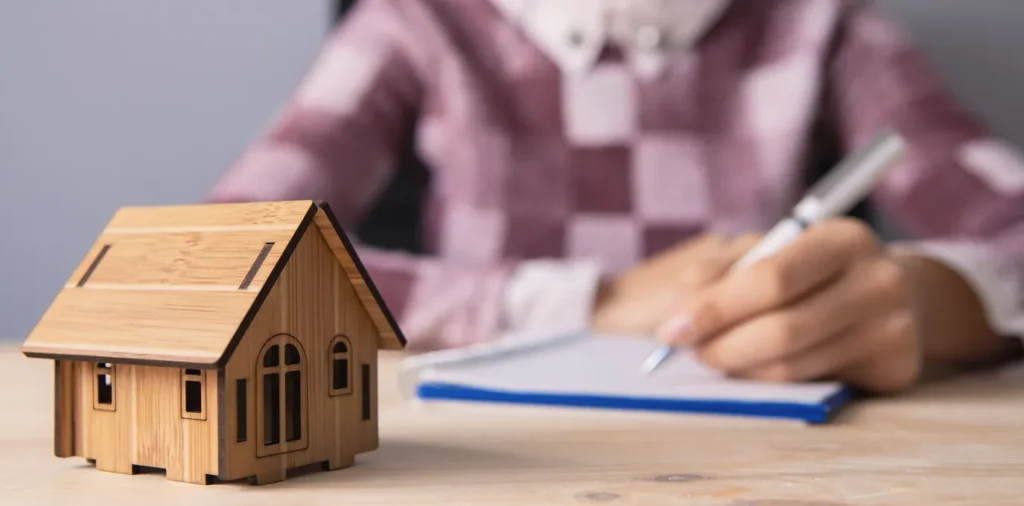A woman signing a contract with a mini house on the table.