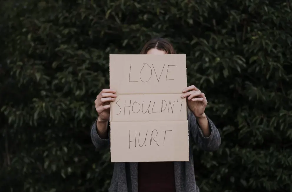 A woman holds a sign that says 'Love shouldn't hurt.