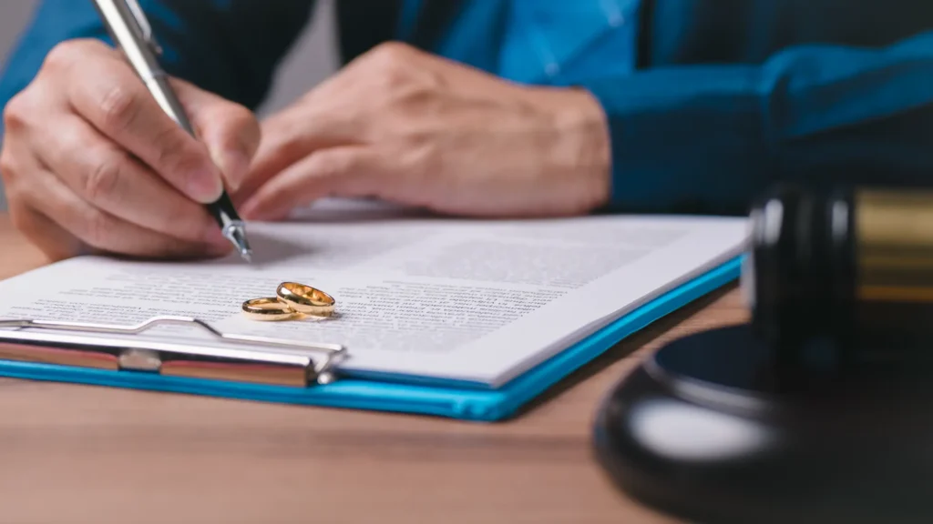 A man signing a divorce decree with wedding rings and a gavel.