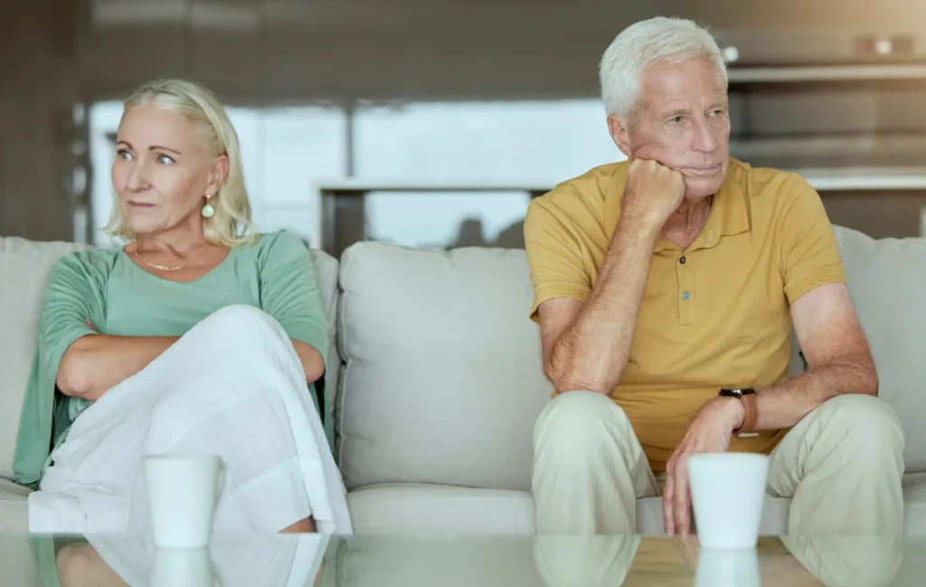 Older couple sitting apart on a couch, looking distant and unhappy, representing gray divorce in Sugar Land.
